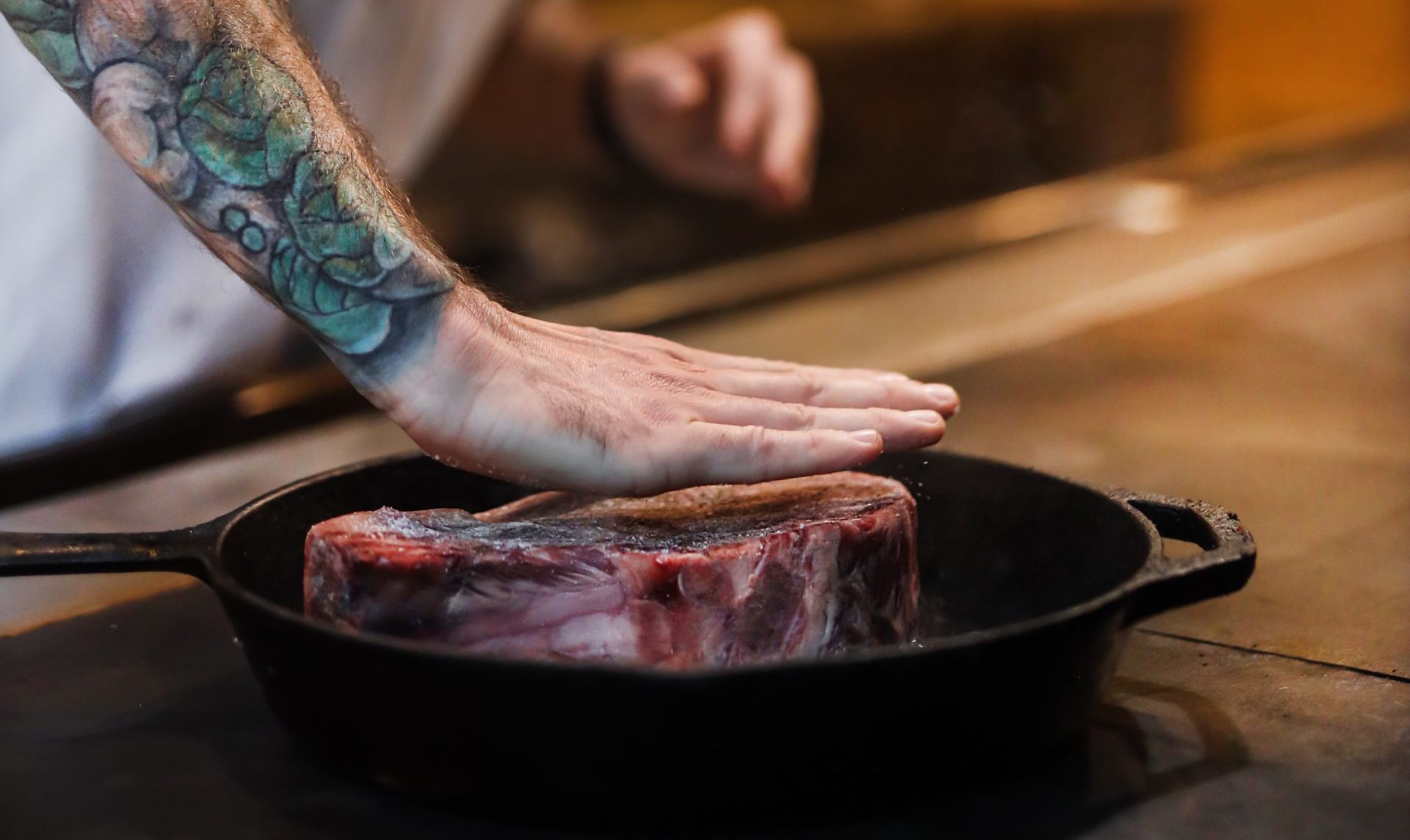 chef pressing down meat in cast iron pan