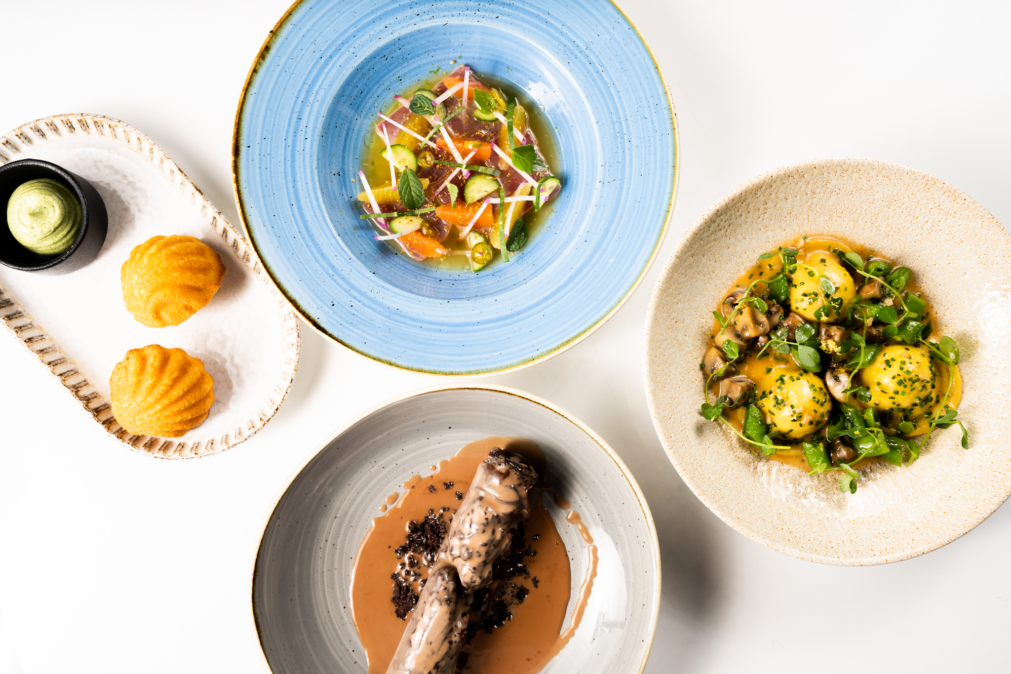 Overhead shot of 4 dishes on plates on a white table