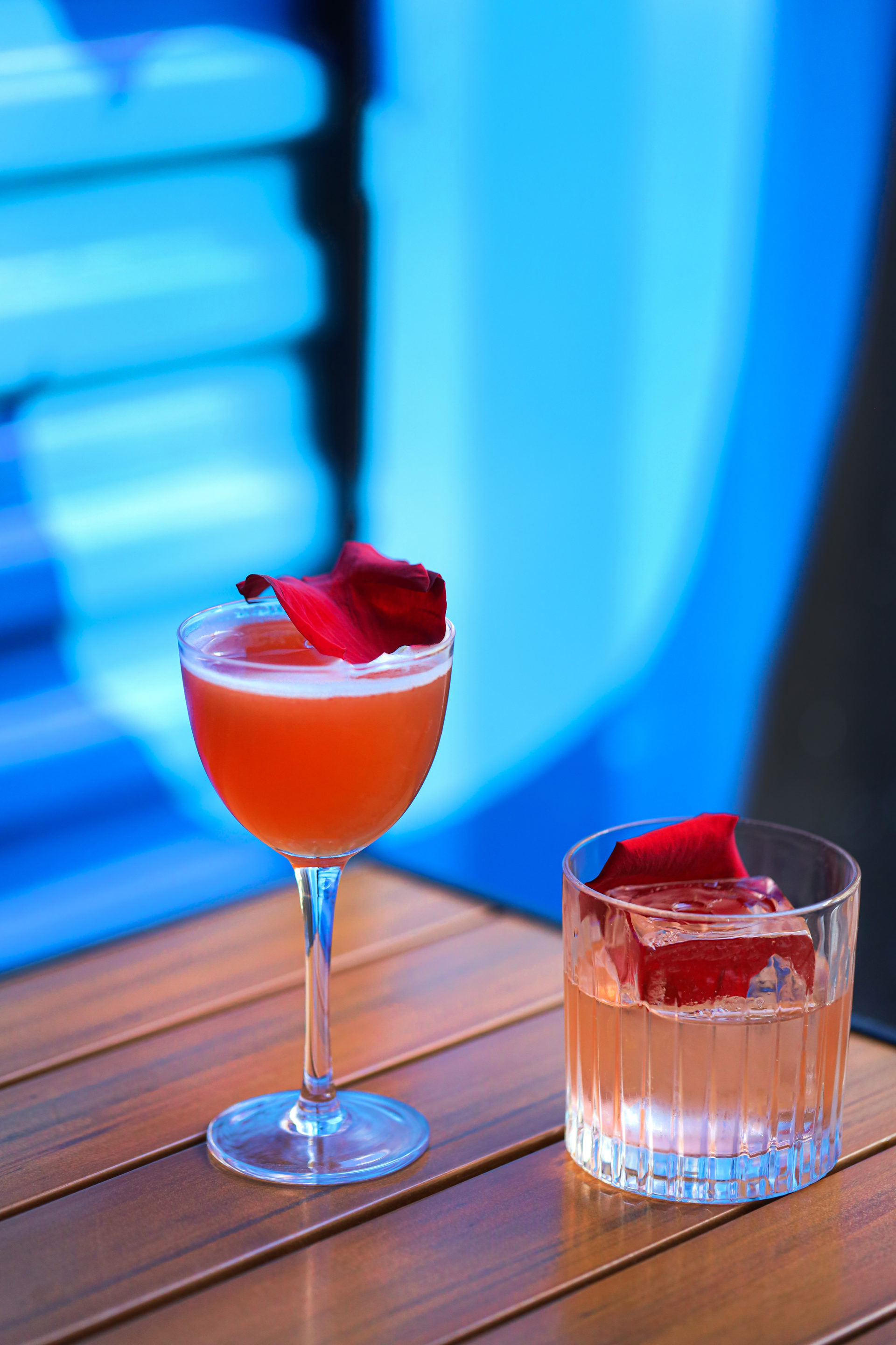two cocktails with rose petals in them placed on table