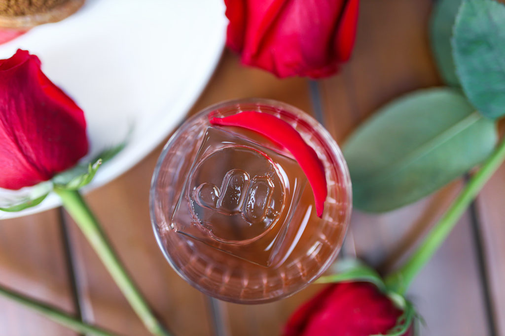 overhead shot of cocktail with large branded ice cube, surrounded by roses