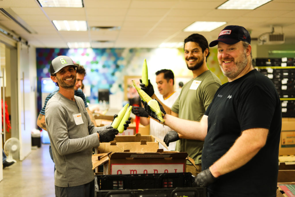 group of men holding corn, smiling at camera