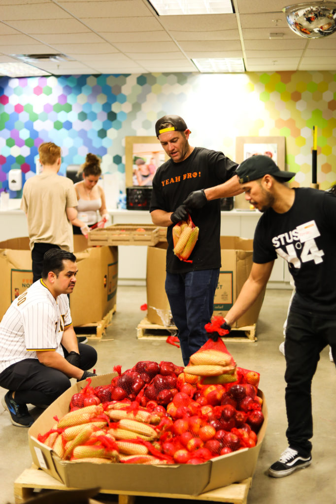 three men loading bags of corn onto a pile of food