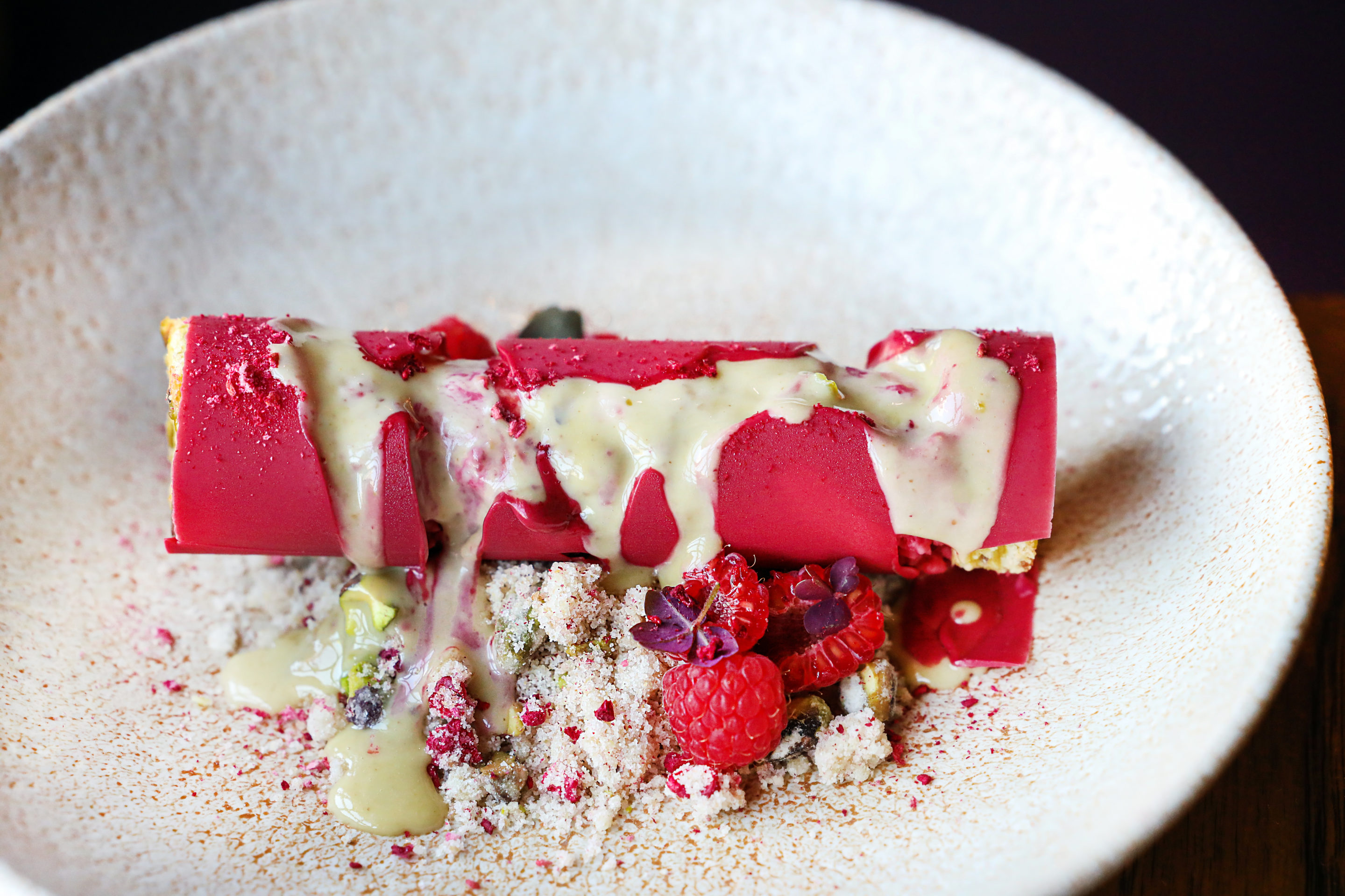 Hot pink cylindrical ice cream dessert with white chocolate poured on top