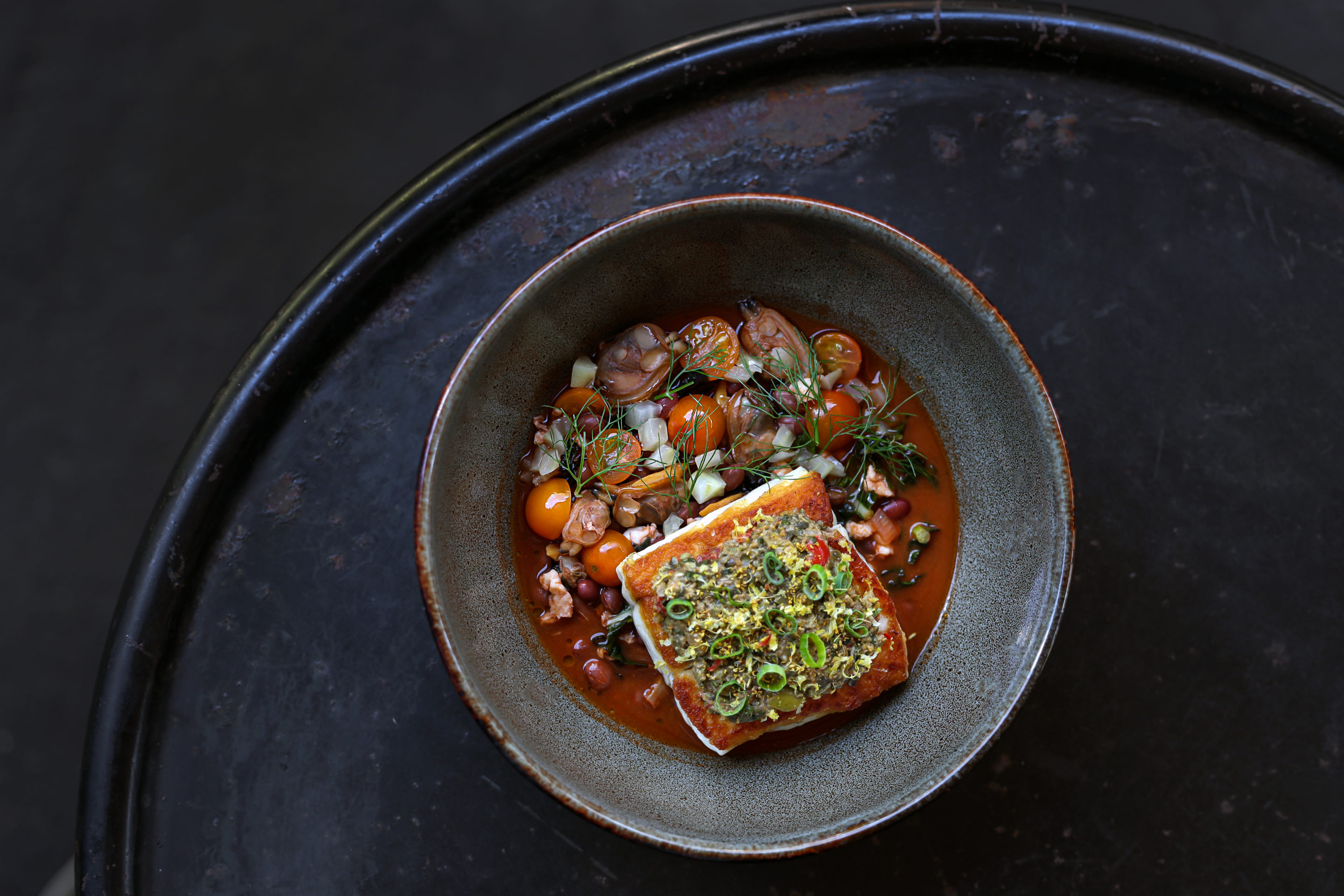 Overhead shot of local catch on a plate with broth and tomatoes