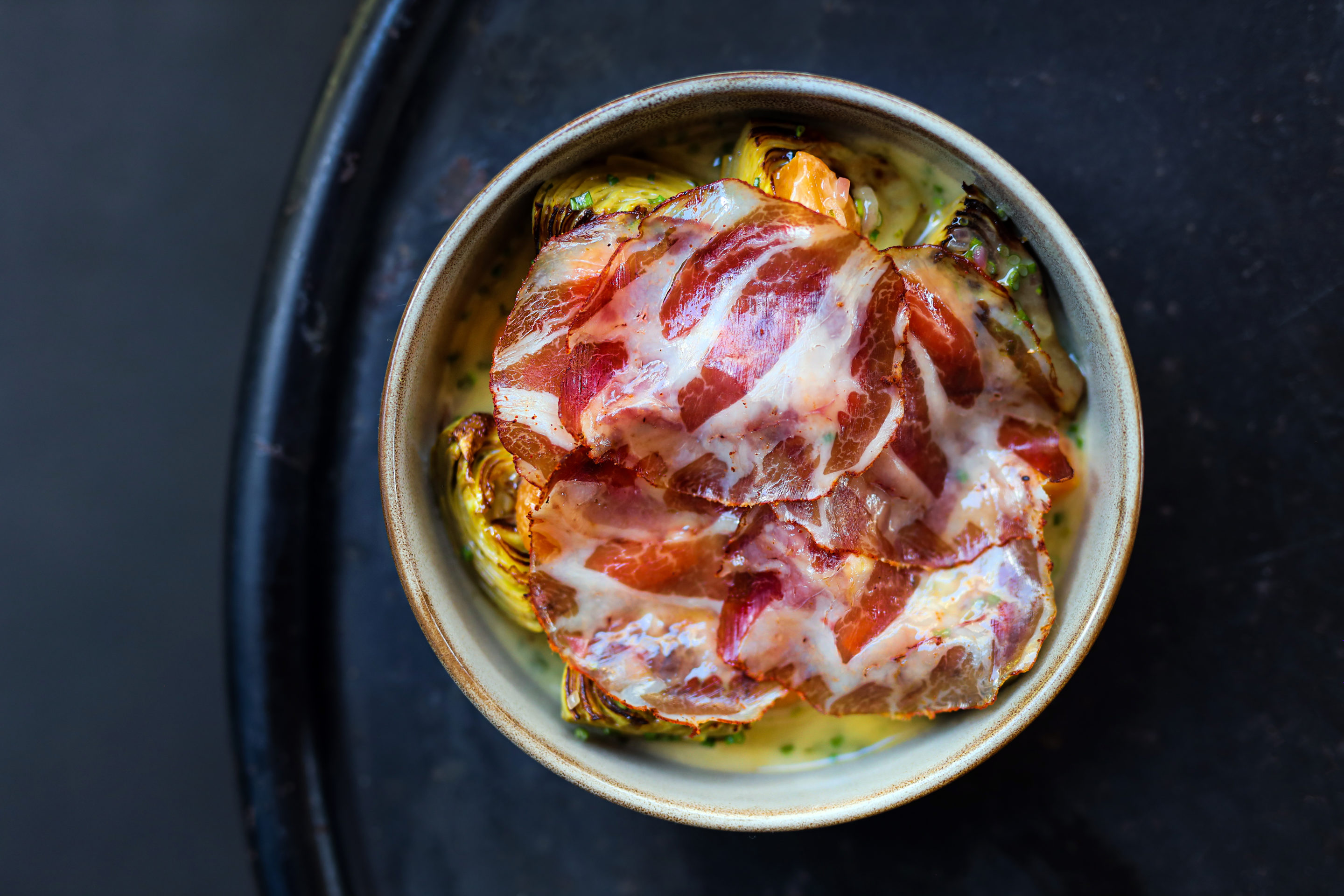 Bowl of brussel sprouts covered with prosciutto in a sauce