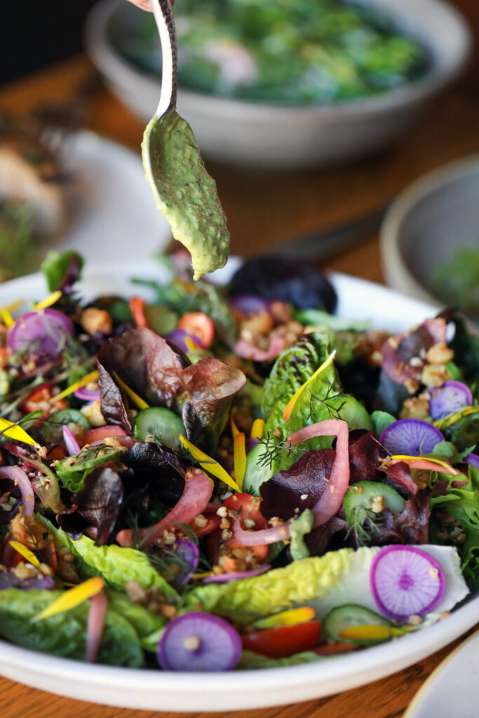 Spoon drizzling dressing over greens