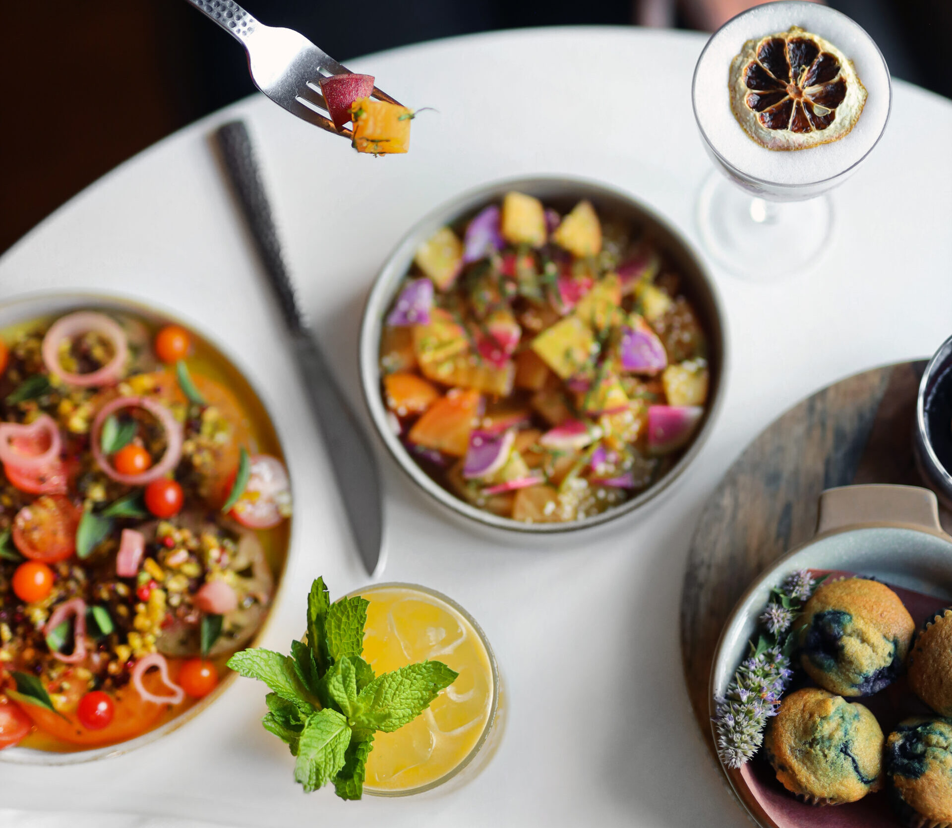 Fork of food being held over brunch items and a cocktail